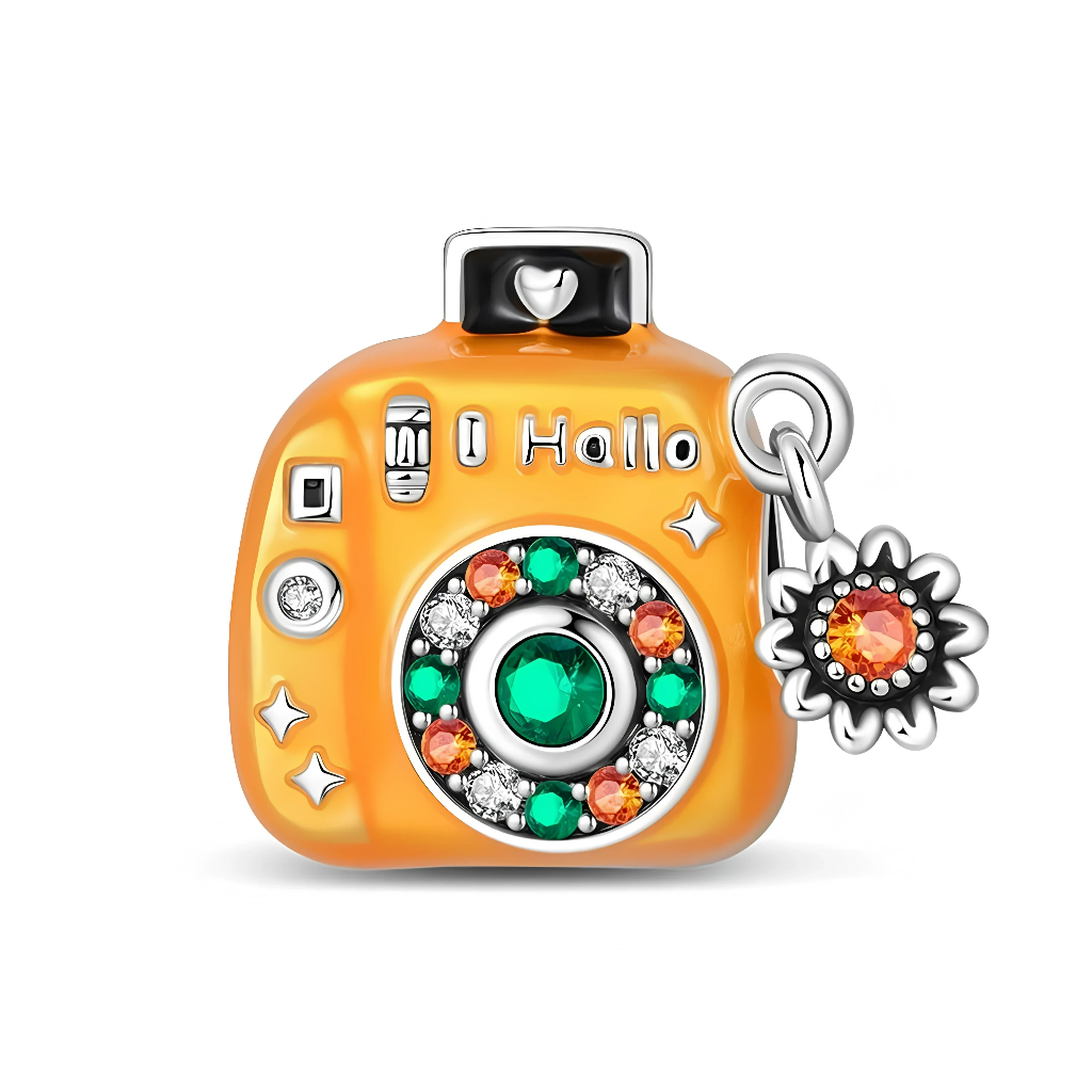 Ce charm amusant prend la forme d’un appareil photo compact orange, décoré comme une citrouille de fête avec de nombreux détails en relief. La façade est ornée d’un grand objectif circulaire pavé de cristaux verts, orangés et transparents, tandis qu’un petit pendentif fleur avec cristal orange est fixé sur le côté pour rappeler un soleil ou un tournesol festif.