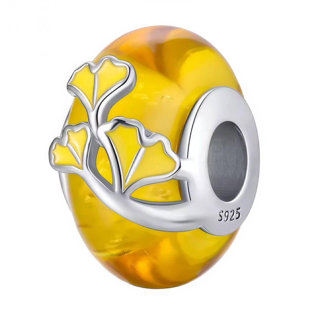 Ce charm marie la transparence vibrante du verre de Murano couleur miel avec un motif de feuilles de ginkgo stylisées, symbole de longévité et de renaissance. Les nuances dorées créent des reflets profonds qui évoquent les feuillages d’octobre, tandis que l’enlacement d’argent poli apporte relief et élégance. Idéal pour des compositions automnales, nature ou zen, il illumine le bracelet d’un éclat chaleureux.
