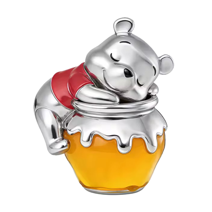 Ce charm met en scène Winnie l’Ourson, l’ours le plus gourmand de la Forêt des Rêves Bleus, confortablement lové contre son pot de miel préféré, dont la résine jaune translucide rappelle la fameuse “hunny” qu’il adore. Son t‑shirt rouge emblématique et son expression tranquille évoquent la douceur, la tendresse et l’enfance, pour un bijou plein de nostalgie et de réconfort.