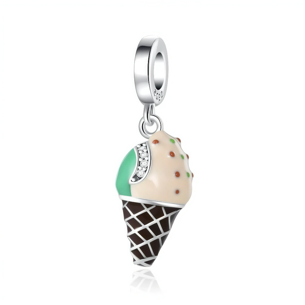 La bélière en argent 925 lisse laisse pendre un cornet façon gaufrette chocolat brune, surmonté d’une boule de glace bicolore crème et vert menthe, décorée de petites pépites colorées. Un fin bandeau pavé de zircons clairs souligne la séparation des saveurs, ajoutant une note scintillante à ce motif de glace très réaliste.