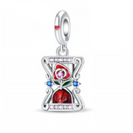 La bélière en argent 925 est lisse avec un petit cœur rouge émaillé sur le côté, d’où descend un cadre de sablier stylisé serti de zirconias roses et transparents en haut et en bas, et de deux pierres bleues au milieu. À l’intérieur du sablier, une rose rouge émaillée avec feuilles vertes se dresse au‑dessus d’un crâne rouge poli, créant un contraste symbolique entre amour et mortalité dans un esprit memento mori romantique.