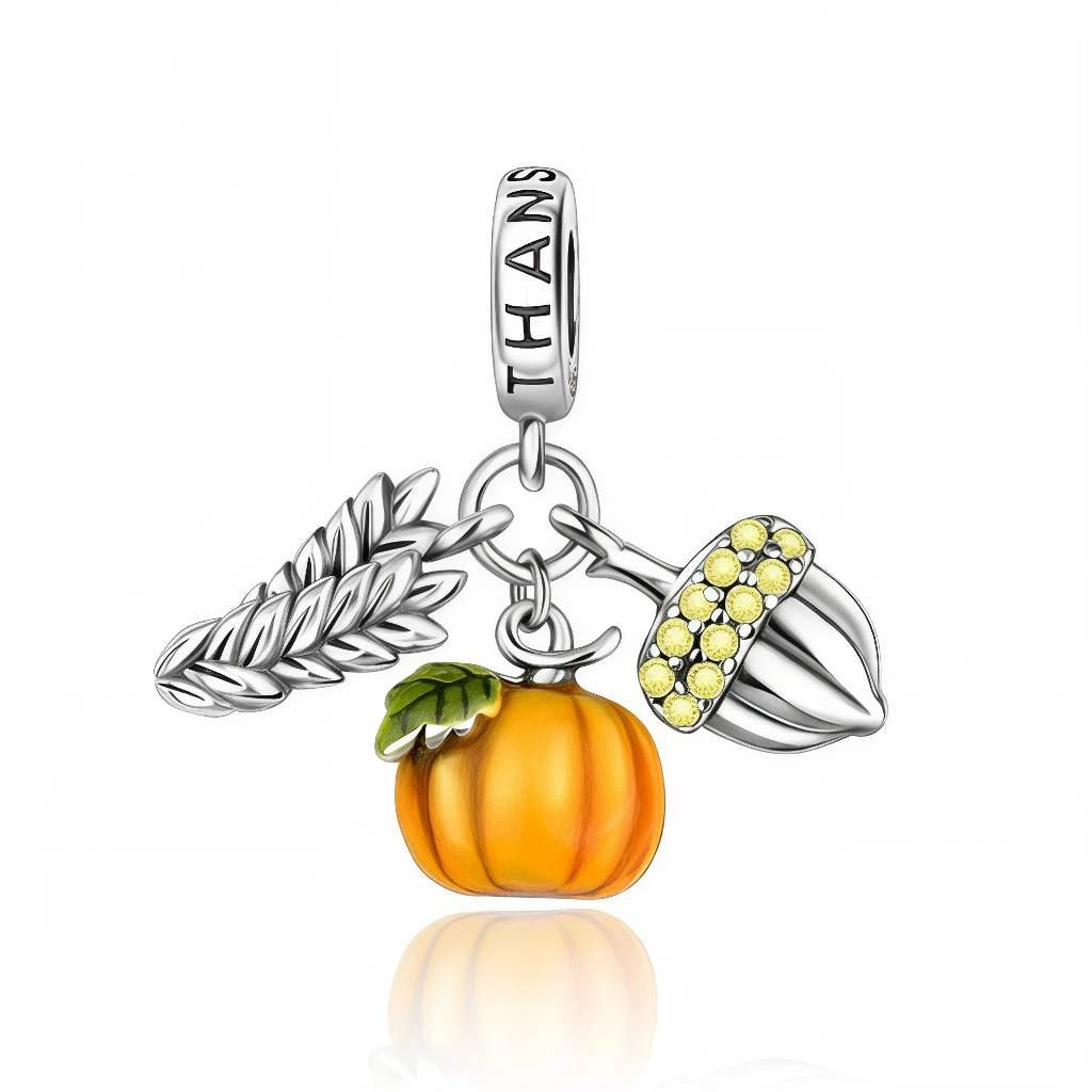La bélière en argent 925 est gravée du mot « THANKS » et relie trois pendentifs mobiles : un épi de blé argenté, une citrouille émaillée orange avec feuille verte et un gland orné de cristaux jaunes sur son capuchon. Les détails texturés du blé et du gland ajoutent du relief tandis que la citrouille apporte une touche chaleureuse de couleur.