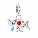 La bélière en argent 925 porte l’inscription « PEACE » et le poinçon S925, d’où pendent trois petits charms : une colombe blanche aux ailes bleu dégradé, une main formant le signe de paix tenant un cœur rouge, et un ruban d’espoir pavé de zircons roses. Chaque élément est articulé sur son anneau, ce qui donne beaucoup de mouvement au bijou et renforce l’idée de paix, d’amour et de soutien aux causes solidaires.