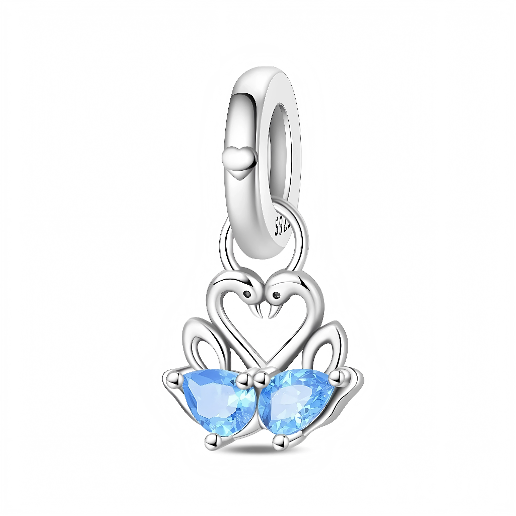 La bélière en argent 925 est lisse avec un petit cœur en relief et relie le pendentif par deux anneaux. Le pendentif montre deux cygnes argentés face à face dessinant un cœur avec leurs cous, tandis que leurs corps sont remplacés par deux pierres bleu clair taille cœur, serties en griffe.