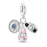 La bélière en argent 925 porte trois petites breloques mobiles : une boussole ronde gravée avec centre pavé de pierres bleues, un appareil photo noir avec un cristal clair en guise d’objectif, et un sac à dos détaillé avec empiècements d’émail rose et un petit cœur sur la poche. L’ensemble évoque un kit complet de globe‑trotter, idéal pour garder au poignet ses souvenirs de road‑trips, randonnées ou city trips.