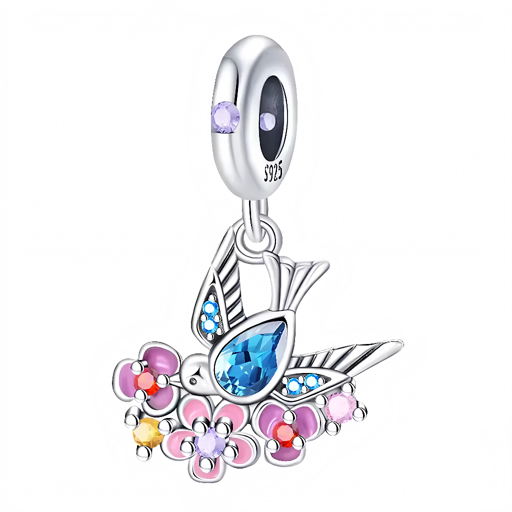 Ce charm célèbre la légèreté et la couleur. Le petit oiseau stylisé arbore des ailes ponctuées de micro‑cristaux bleus et un corps sublimé par une pierre centrale bleu azur taille poire. Il survole un parterre de fleurs roses, violettes et jaunes rehaussées de cabochons scintillants. La bélière est sertie d’une gemme lavande qui renforce l’harmonie pastel. Idéal pour un thème nature, bohème ou renouveau.