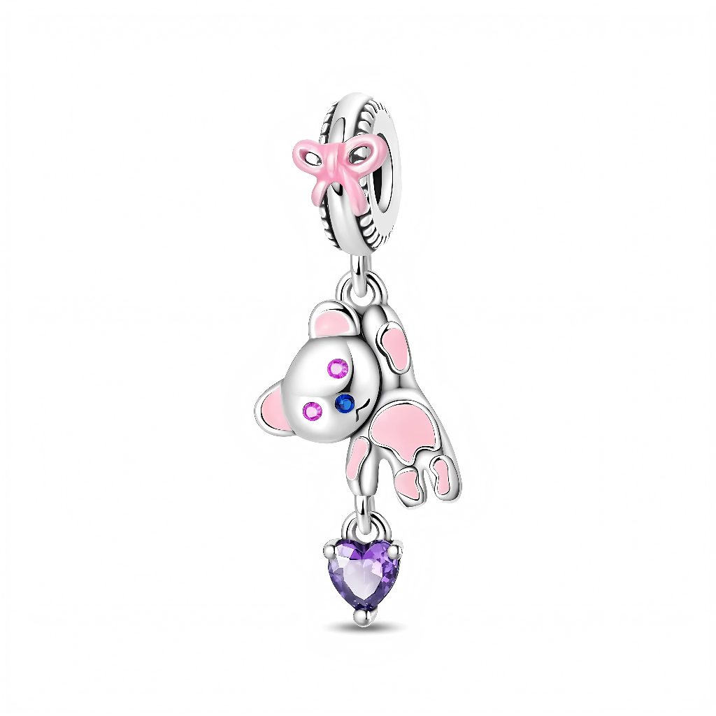 La bélière en argent 925 est décorée d’un nœud rose en émail, donnant un aspect délicat et enfantin. L’ourson articulé, rehaussé d’émail rose sur les pattes et les oreilles, possède des yeux pavés de cristaux rose et bleu, tandis qu’un cœur en zircon violet en forme de pierre de taille pend en dessous.