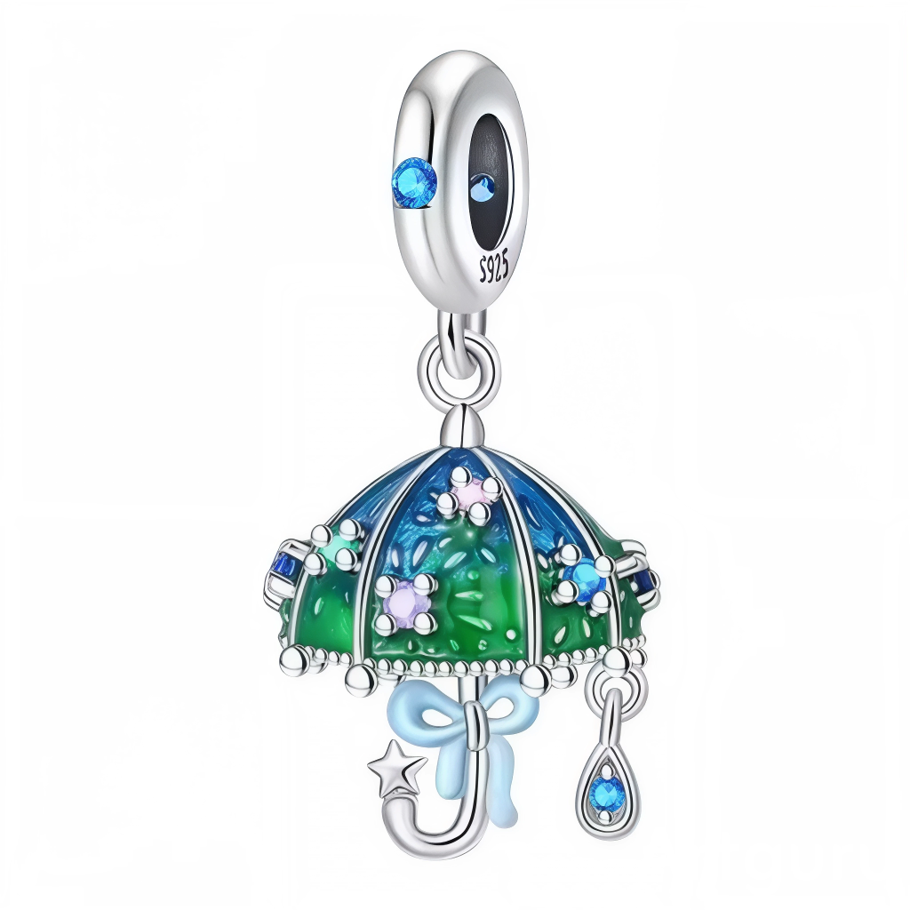 Ce charm capture la poésie des jours de pluie colorés. La coupole émaillée bleu océan et vert prairie est soulignée de nervures argentées et parsemée de petites fleurs scintillantes. Au bord, un nœud pastel habille la poignée en J, tandis qu’une goutte sertie et une étoile stylisée apportent du mouvement. La bélière est sertie d’un cristal bleu qui rappelle l’ensemble, parfait pour un thème météo, printemps ou chance.