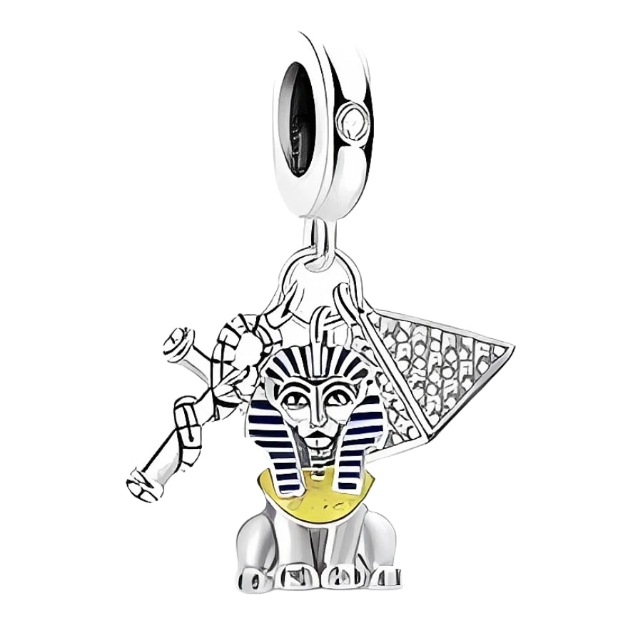Ce charm met en lumière une figure de sphinx assis en argent 925, rehaussée de rayures émaillées bleu nuit et d’un plastron jaune lumineux pour une allure majestueuse. Il est accompagné d’une pyramide stylisée et d’un fouet croisé, créant un ensemble riche en détails qui évoque les mystères et la grandeur des civilisations anciennes.