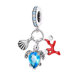 Ce charm capture la beauté des fonds marins avec trois éléments mobiles. La tortue, pièce centrale, brille grâce à une pierre bleu lagon facettée et à des nageoires finement gravées; elle est accompagnée d’un coquillage argent brossé et d’un corail rouge laqué au relief stylisé. La bélière pavée de cristaux bleu ciel rappelle la couleur de l’océan, idéale pour un thème vacances, plongée ou souvenirs de bord de mer.