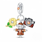 Ce charm pendentif en argent 925 raconte une petite scène de vie à la campagne avec trois breloques colorées : un épouvantail souriant, un grand tournesol jaune et un appareil photo vintage. Le tout est suspendu à un anneau lisse orné d’un petit cristal orange, ce qui ajoute une touche lumineuse et chaleureuse.
