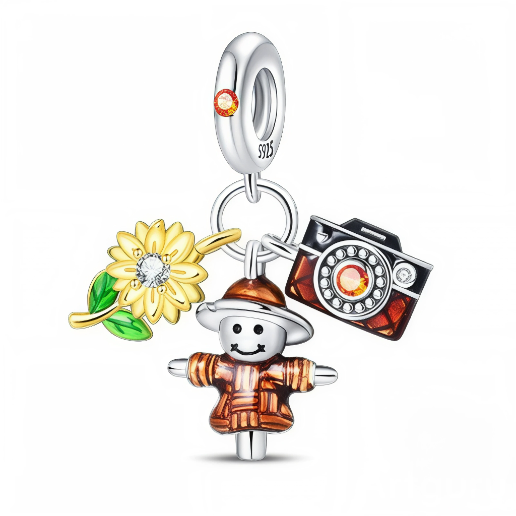 Ce charm pendentif en argent 925 raconte une petite scène de vie à la campagne avec trois breloques colorées : un épouvantail souriant, un grand tournesol jaune et un appareil photo vintage. Le tout est suspendu à un anneau lisse orné d’un petit cristal orange, ce qui ajoute une touche lumineuse et chaleureuse.