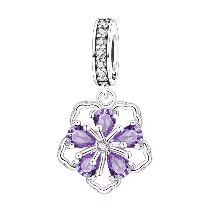 Ce charm met en valeur une fleur graphique composée de cinq pétales cœur facettés violet améthyste, retenus par un délicat serti griffe autour d’un centre scintillant blanc. La monture ajourée en argent dessine un contour léger, tandis que la bélière entièrement pavée de zircons clairs ajoute une ligne de lumière supplémentaire sur le bracelet. Une pièce élégante et féminine, parfaite pour illuminer une composition florale ou romantique.
