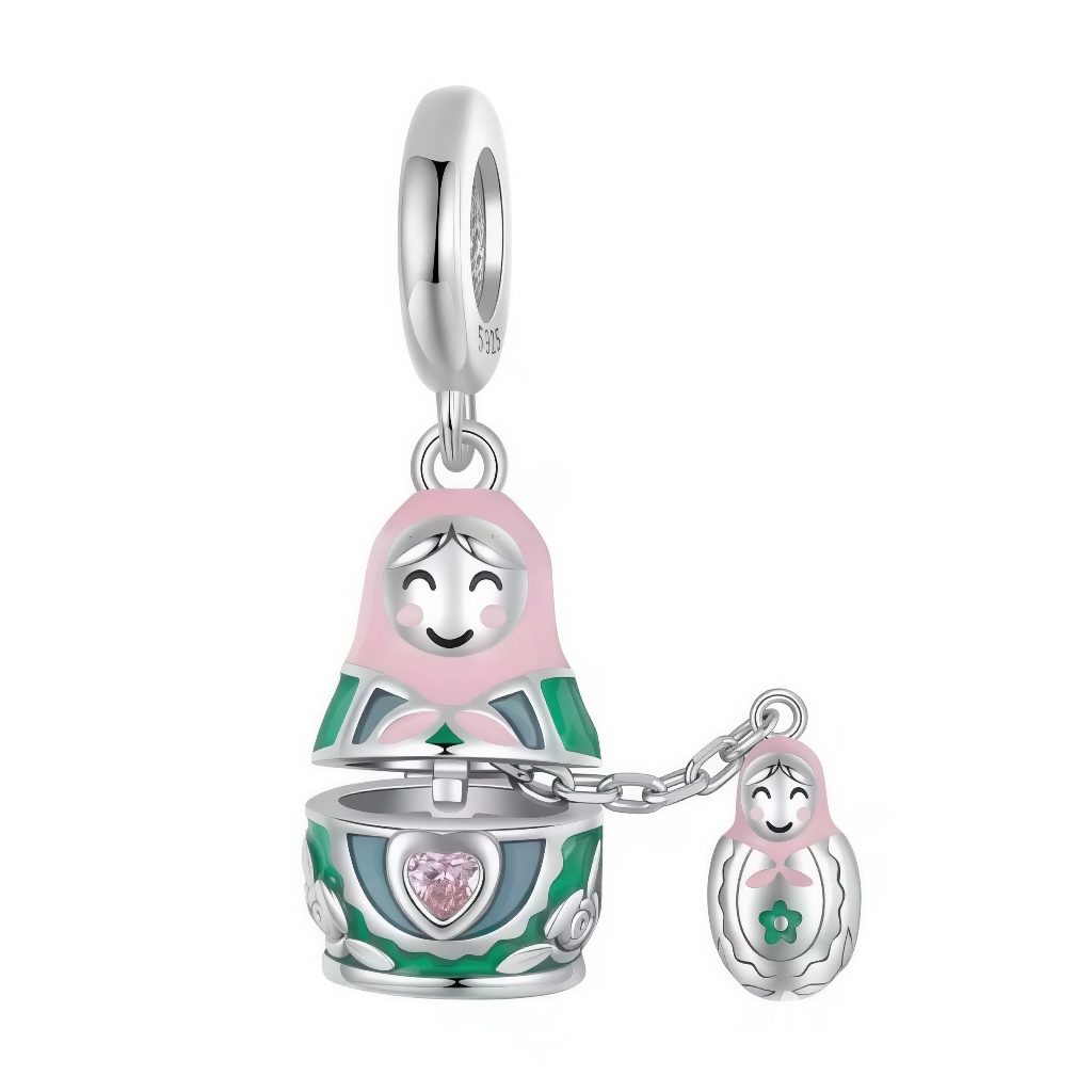 Ce charm pendentif attendrissant met en scène une grande poupée matriochka argentée aux émaux rose et vert, qui s’ouvre pour révéler un cœur facetté rose au centre de son buste. Reliée par une délicate chaînette, une petite matriochka assortie pend gracieusement à ses côtés, créant un duo mère‑enfant plein de tendresse. L’anneau supérieur rond permet une fixation fluide sur les bracelets.