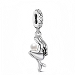 Ce charm en métal argenté représente une jeune sirène assise, les jambes croisées et la longue chevelure ondulée retombant dans son dos, serrant contre elle une perle ronde et lumineuse. Le pendentif est suspendu à un anneau décoré de motifs de coquillages et de bulles, ce qui renforce l’inspiration marine et donne du relief au bijou.