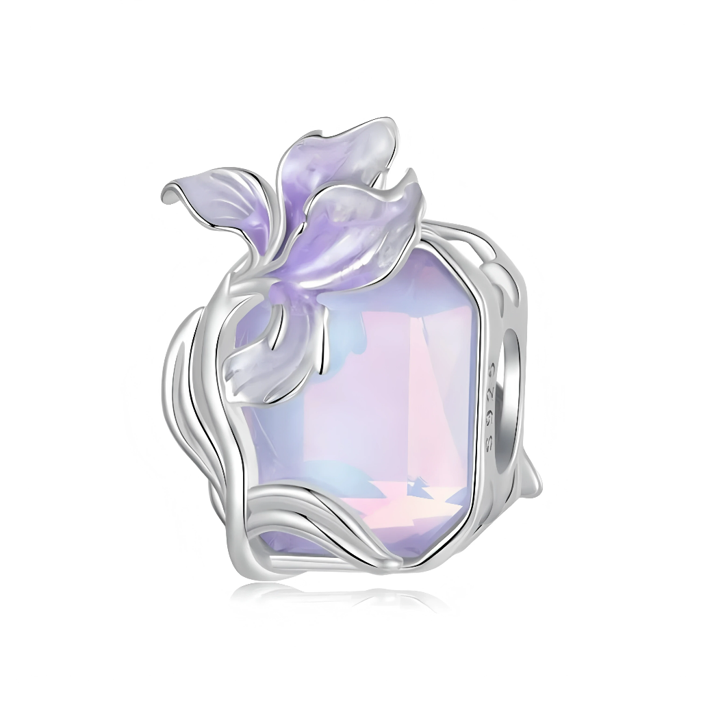 Ce charm en argent 925 met en scène une grande pierre facettée aux reflets mauves et opalescents, entourée de tiges sinueuses qui dessinent un serti façon lianes. Une orchidée délicate, aux pétales en émail violet translucide, semble éclore sur le dessus du bijou, donnant une allure féerique et raffinée.