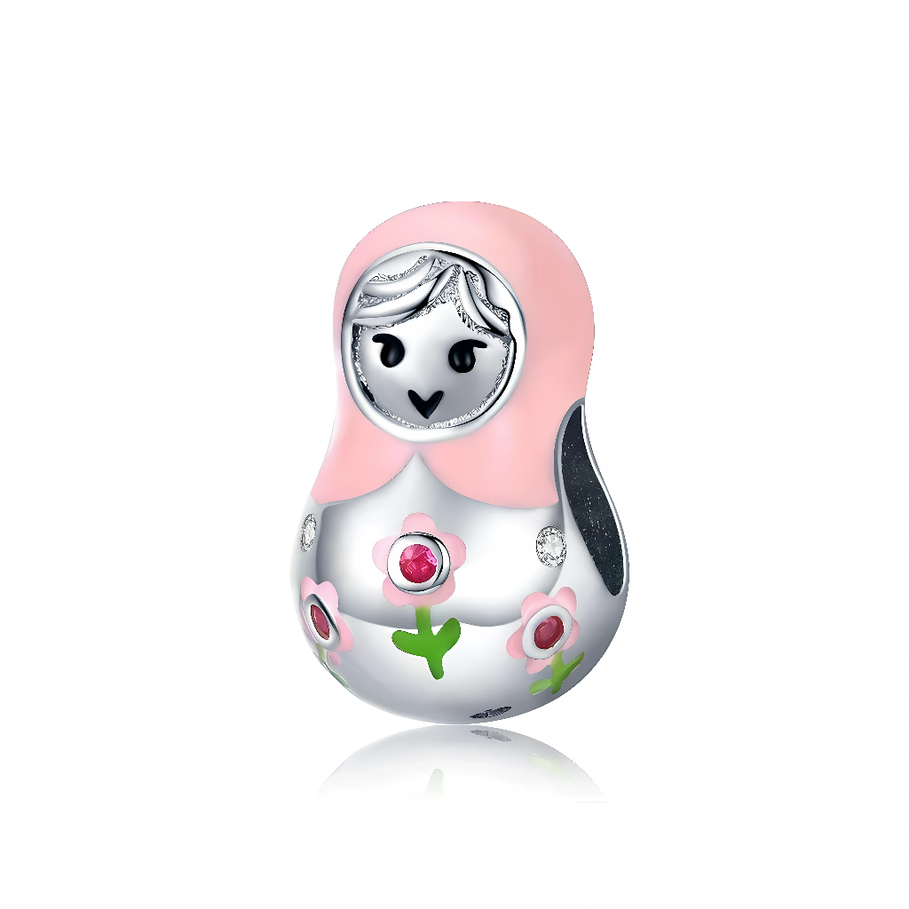 Ce charm en argent 925 représente une adorable poupée matriochka stylisée, coiffée d’un foulard rose pâle et au visage minimaliste noir et blanc. Son corps est décoré de petites fleurs roses et vertes, dont la fleur centrale est ornée d’un cristal rose qui apporte une touche lumineuse et féminine.